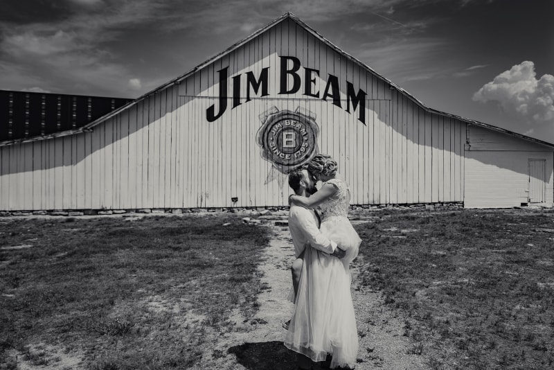 wedding Photographer, a bride holds the flower girl in her arms before a Jim Beam Warehouse