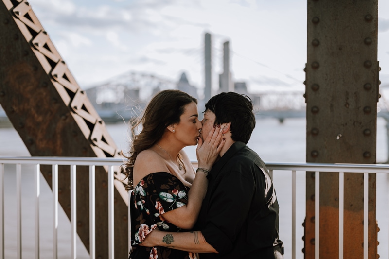 Elopement Photographer, two partners kiss on a bridge, the cityscape behind them