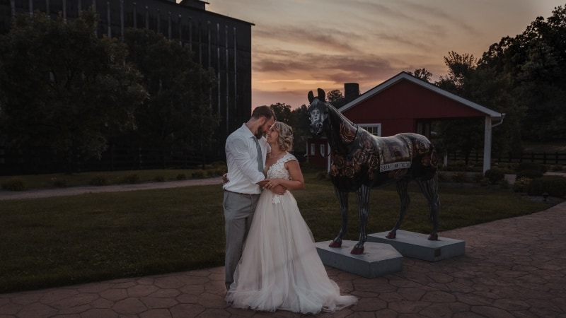 Wedding Photographer, a bride and groom embrace before barn structures and a statue of a horse